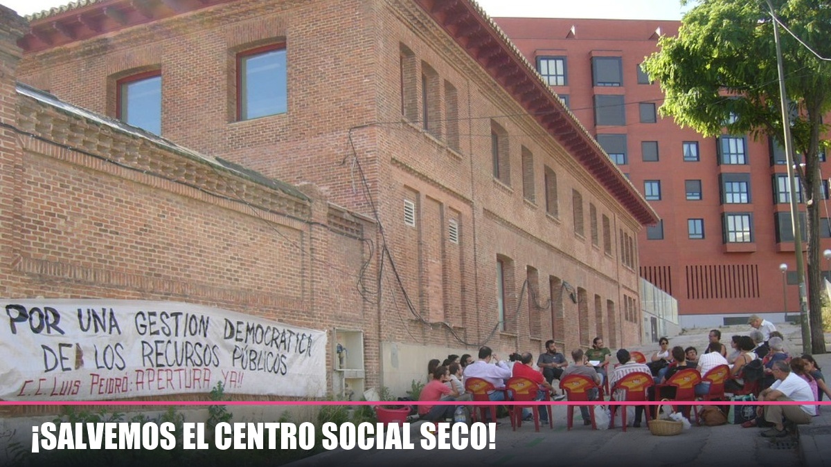 ¡Salvemos el Centro Social Seco! Fotografía de la asamblea vecinal frente al Centro Social Seco en Luis Peidró con el lema y la pancarta por una gestión democrática de los recursos públicos.